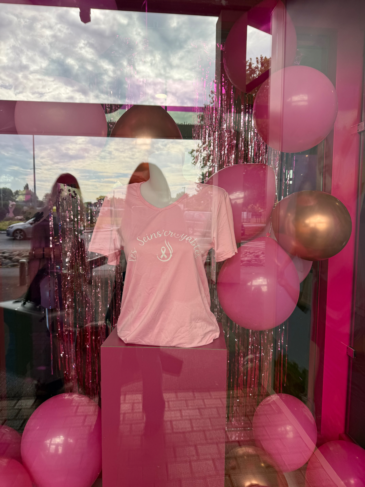 Vitrine décorée de ballons roses avec le t-shirt Les Seins’Croyables